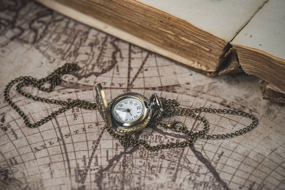 Close-up of an antique pocket watch on a vintage map beside an old book, evoking a sense of history.